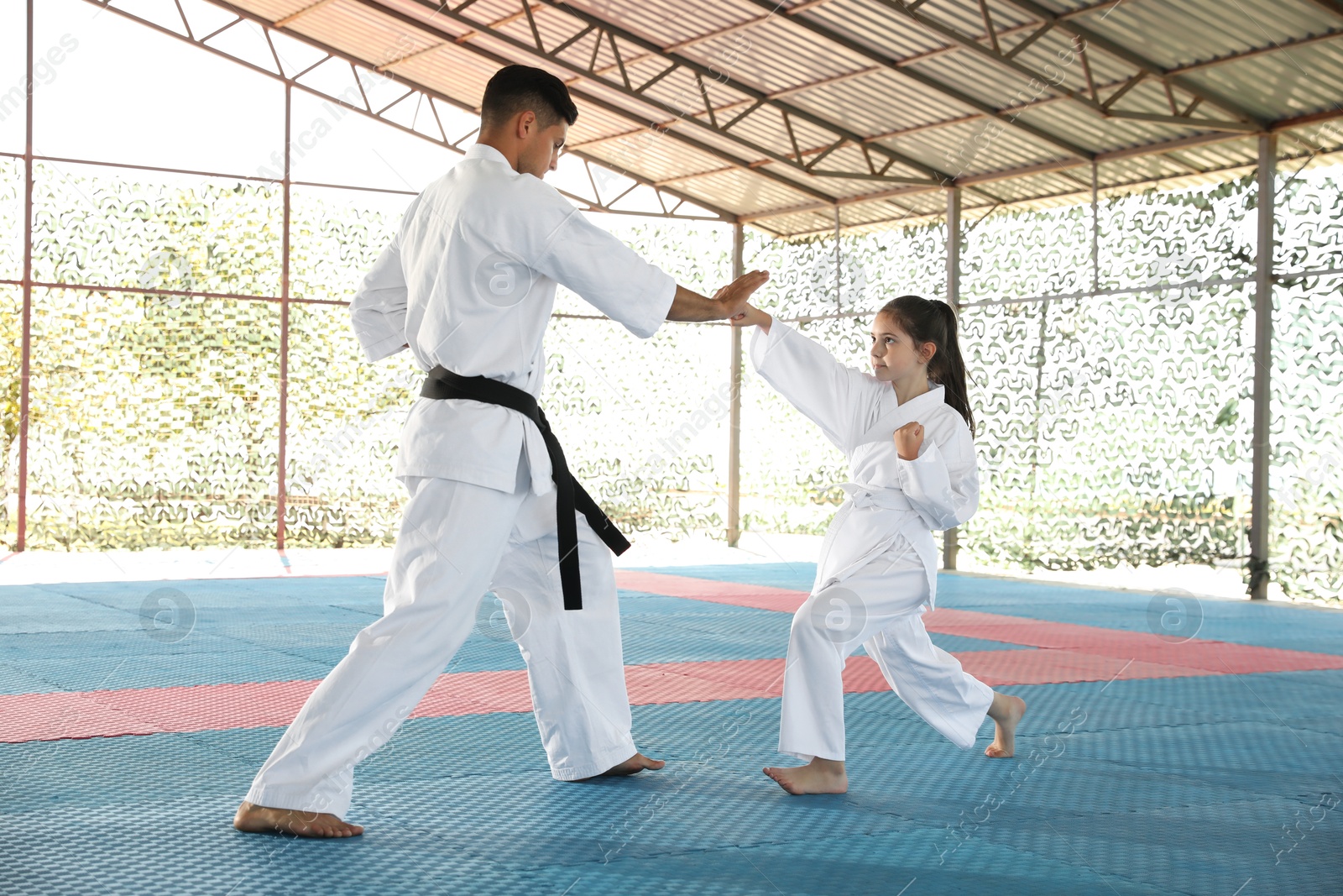 Photo of Girl practicing karate with coach on tatami outdoors