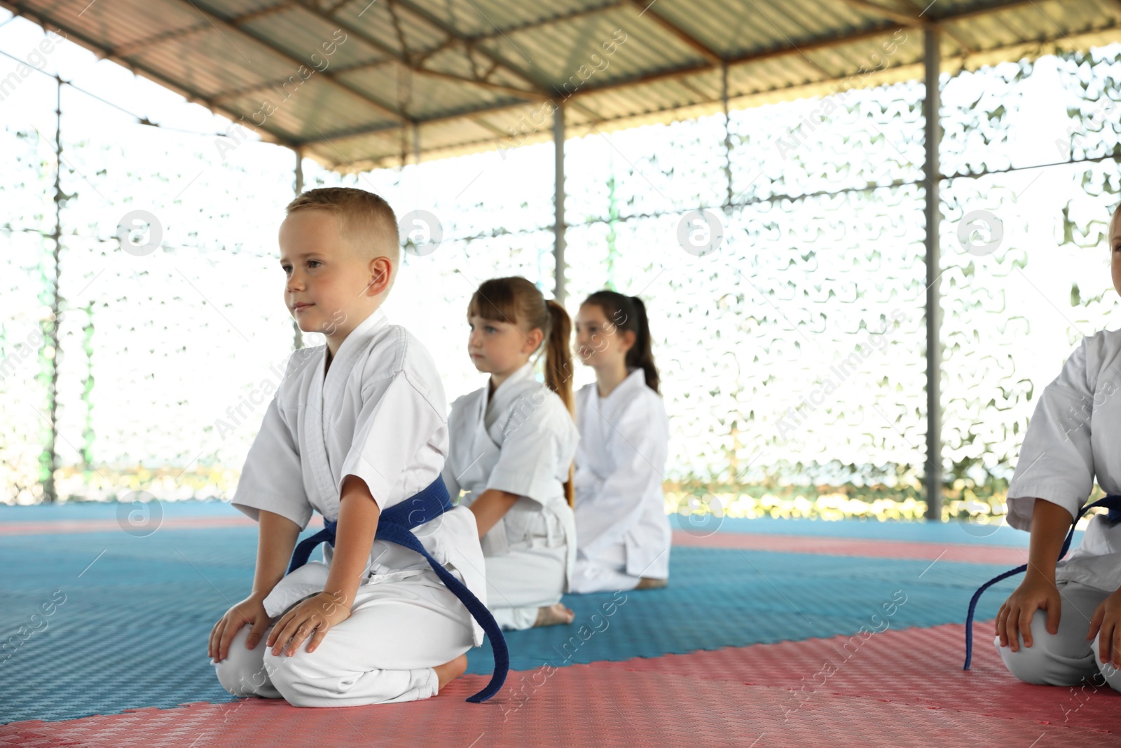 Photo of Children in kimono sitting on tatami outdoors. Karate practice