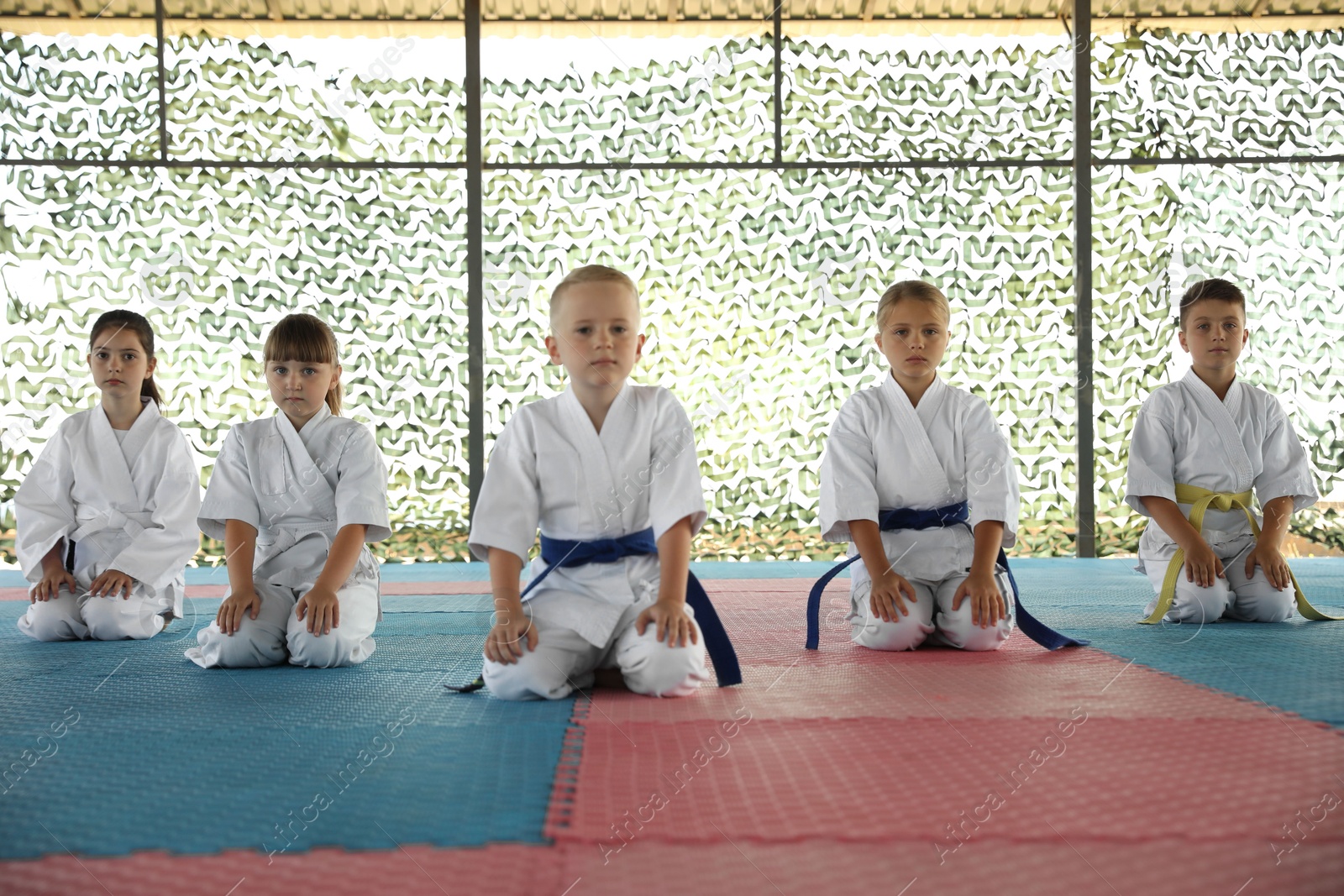 Photo of Children in kimono sitting on tatami outdoors. Karate practice