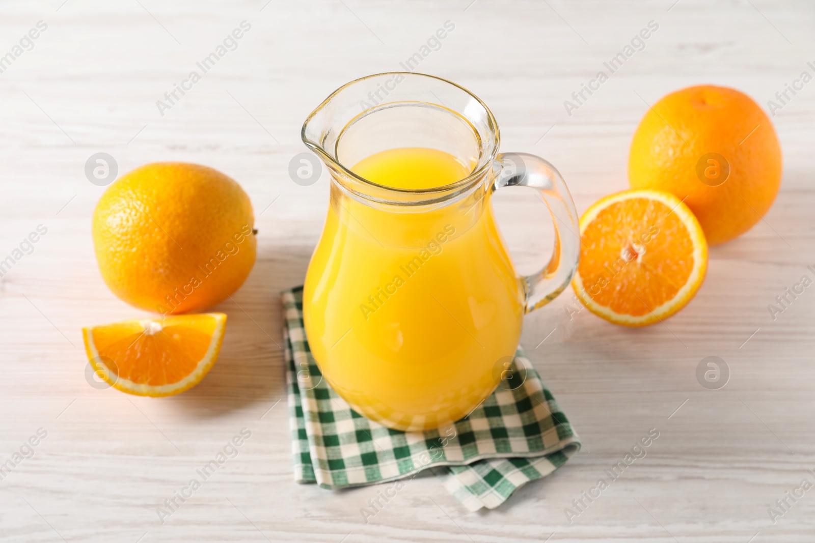 Photo of Tasty orange juice in glass jug and fresh fruits on white wooden table