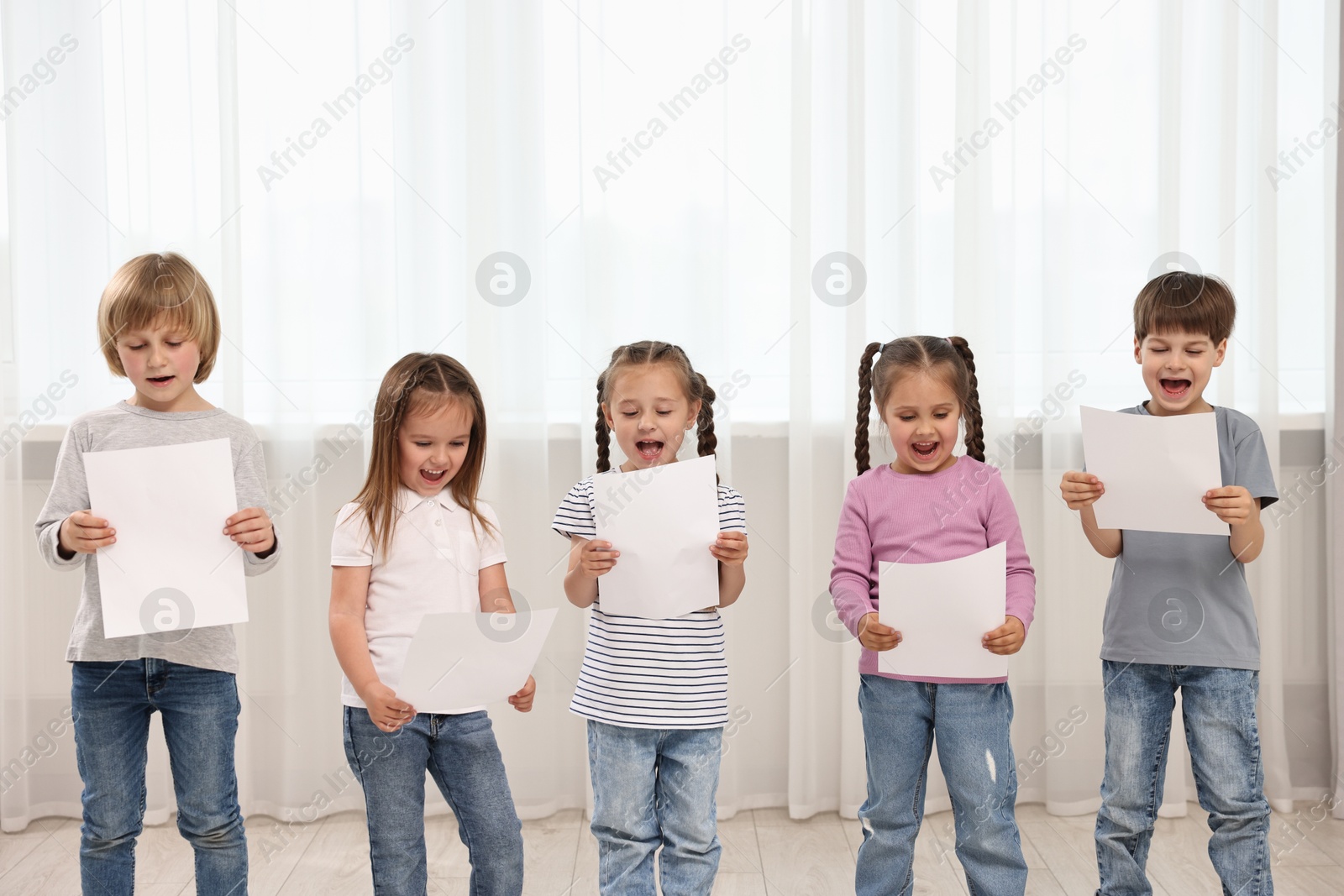 Photo of Group of children with sheets of paper singing indoors