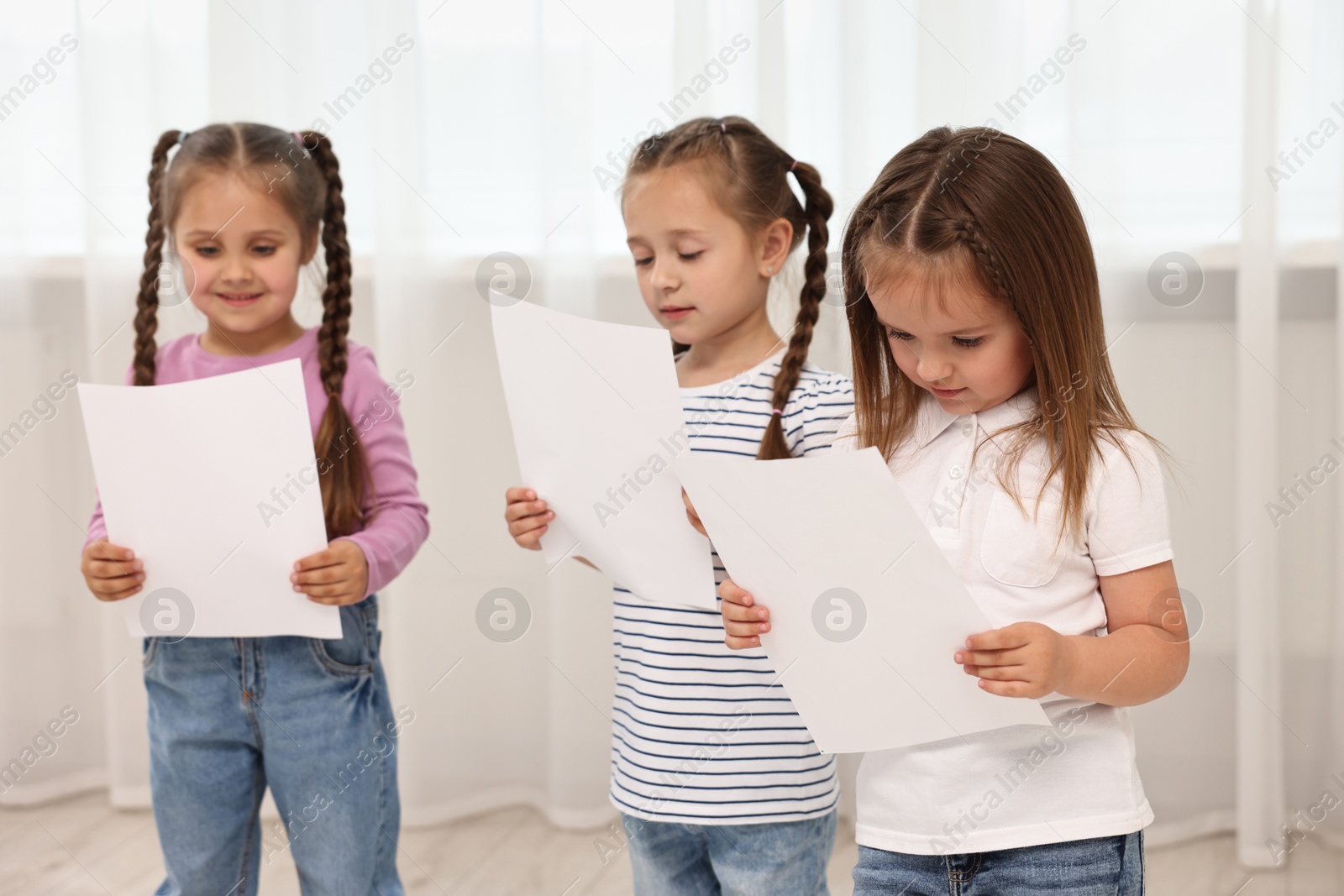 Photo of Cute little children with sheets of paper singing indoors