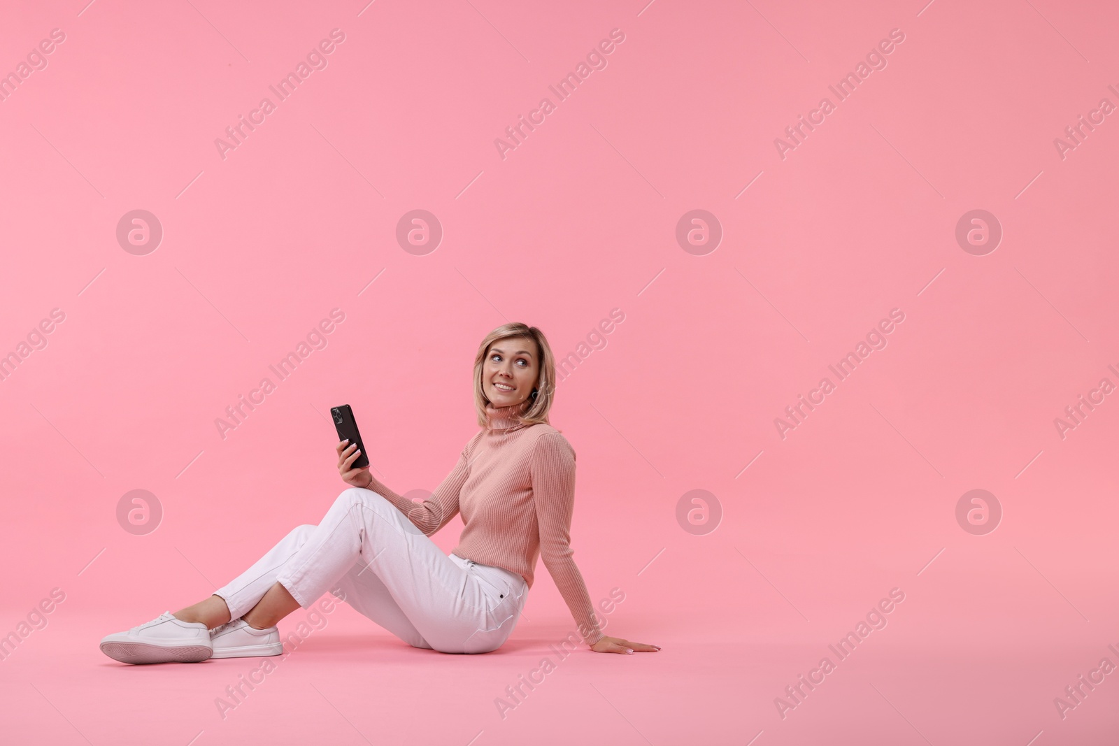 Photo of Happy woman with phone on pink background, space for text