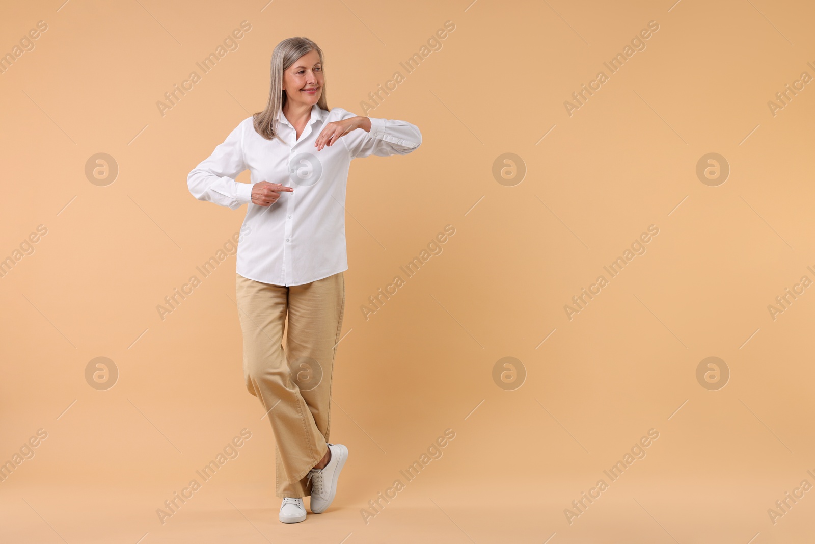 Photo of Happy senior woman pointing on beige background, space for text