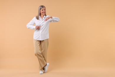 Happy senior woman pointing on beige background, space for text