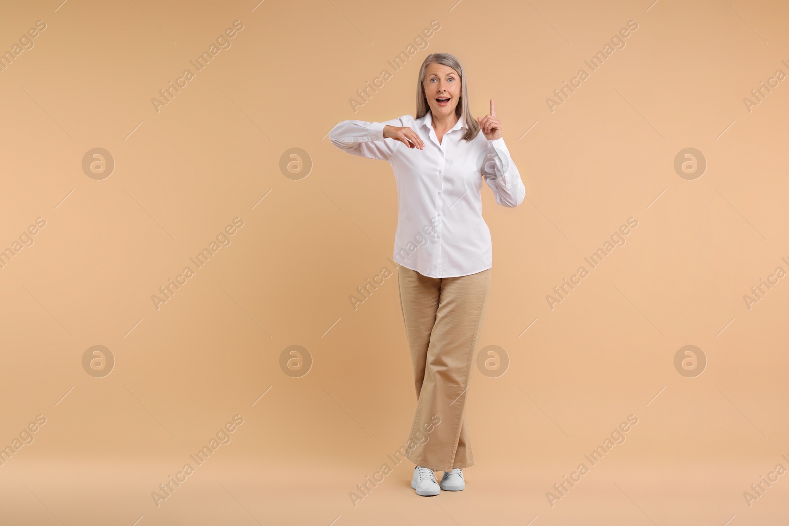 Photo of Happy senior woman pointing on beige background