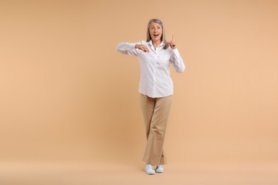 Happy senior woman pointing on beige background