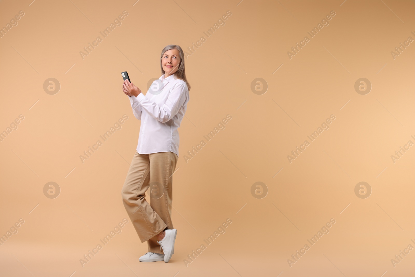 Photo of Senior woman with phone on beige background, space for text