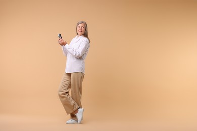 Senior woman with phone on beige background, space for text