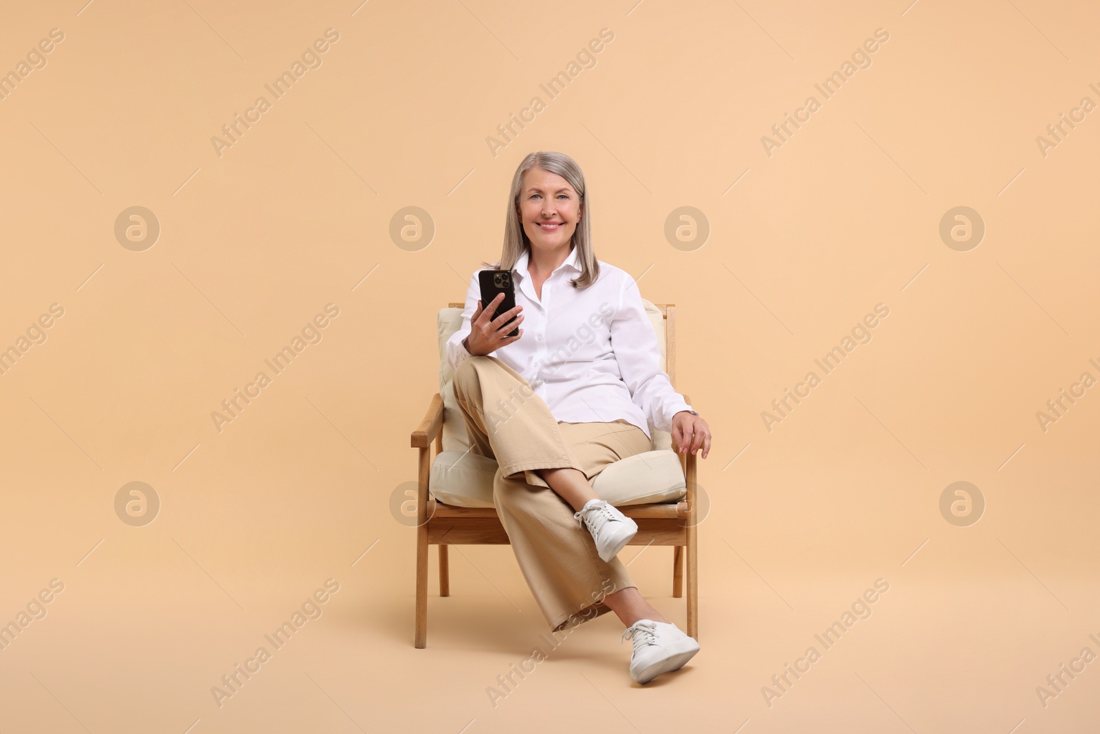 Photo of Senior woman with phone on armchair against beige background