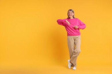 Photo of Happy senior woman pointing on orange background, space for text