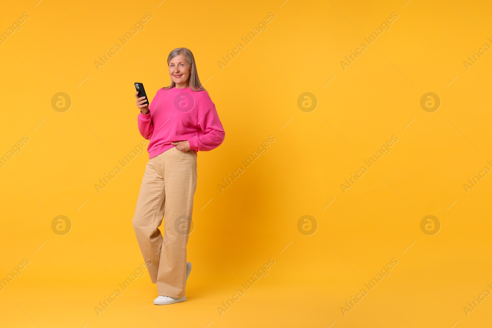 Photo of Senior woman with phone on orange background, space for text