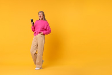 Photo of Senior woman with phone on orange background, space for text