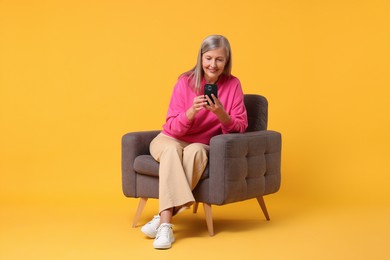 Senior woman with phone on armchair against orange background