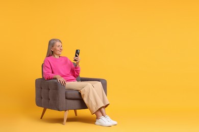 Photo of Senior woman with phone on armchair against orange background, space for text