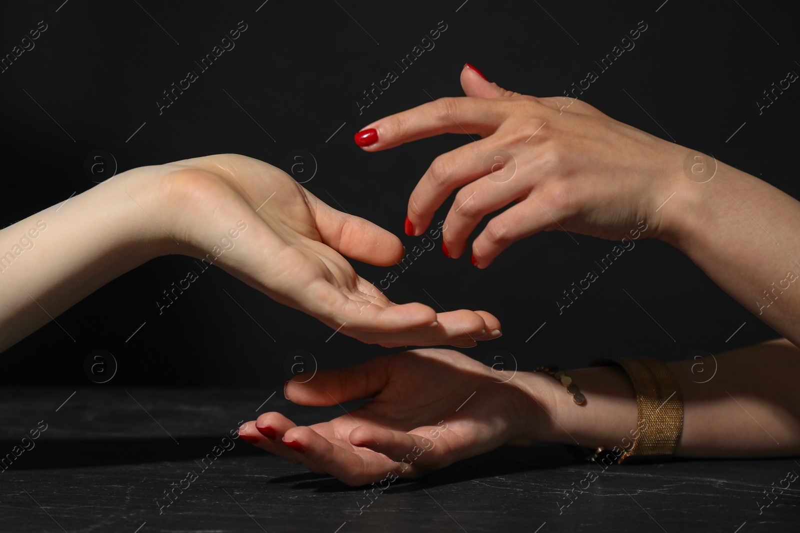 Photo of Fortune teller reading lines on woman's palm at dark grey table, closeup. Chiromancy