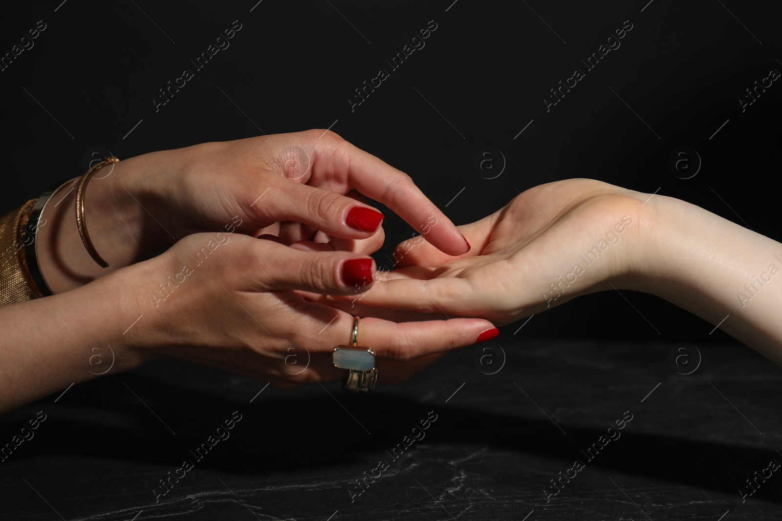 Photo of Fortune teller reading lines on woman's palm at dark grey table, closeup. Chiromancy