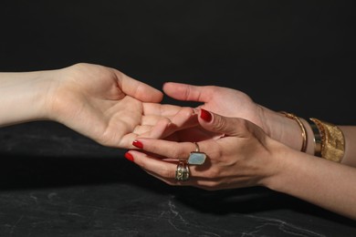 Fortune teller reading lines on woman's palm at dark grey table, closeup. Chiromancy
