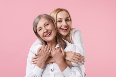 Family portrait of young woman and her mother on pink background