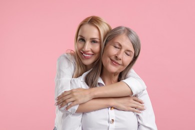 Family portrait of young woman and her mother on pink background