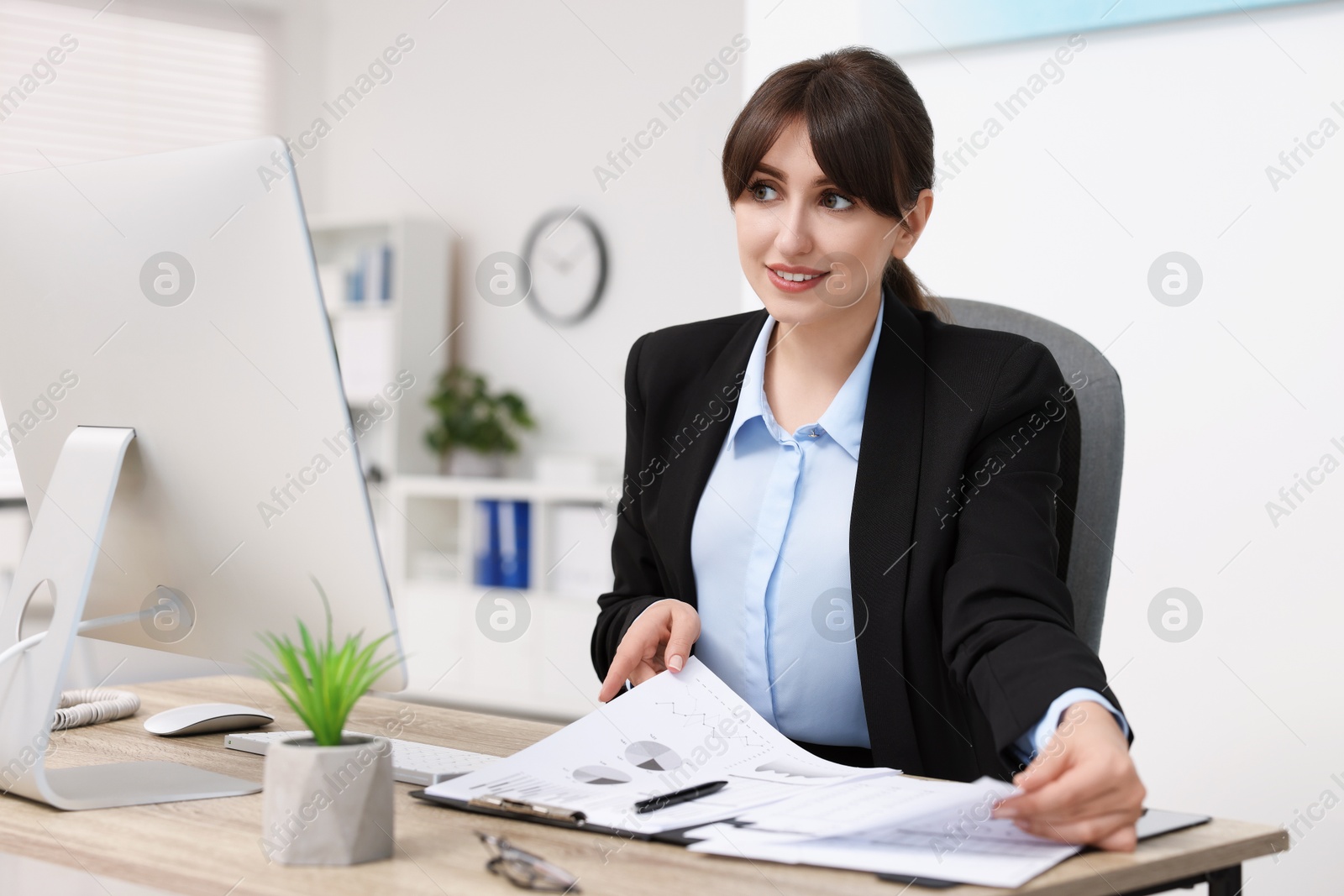 Photo of Smiling secretary doing paperwork at table in office