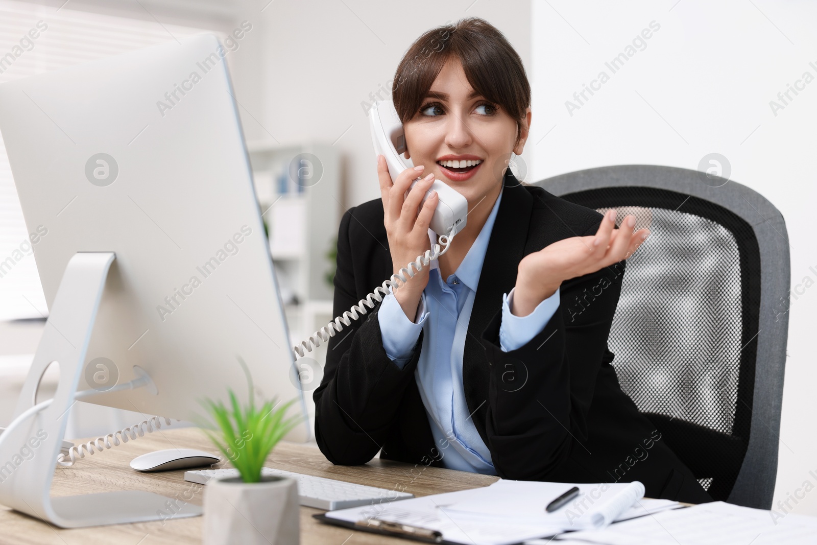 Photo of Smiling secretary talking on telephone at table in office