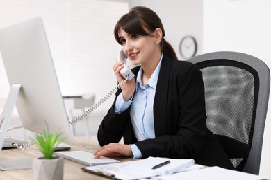 Smiling secretary talking on telephone at table in office