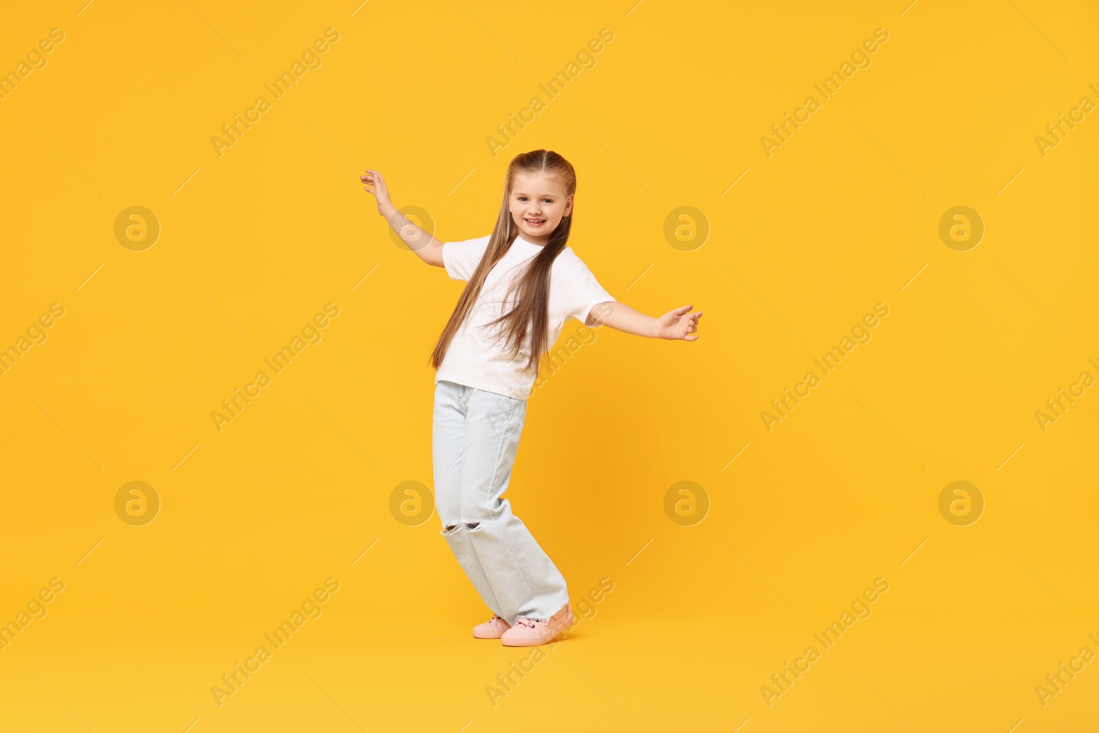 Photo of Cute little girl dancing on yellow background, space for text