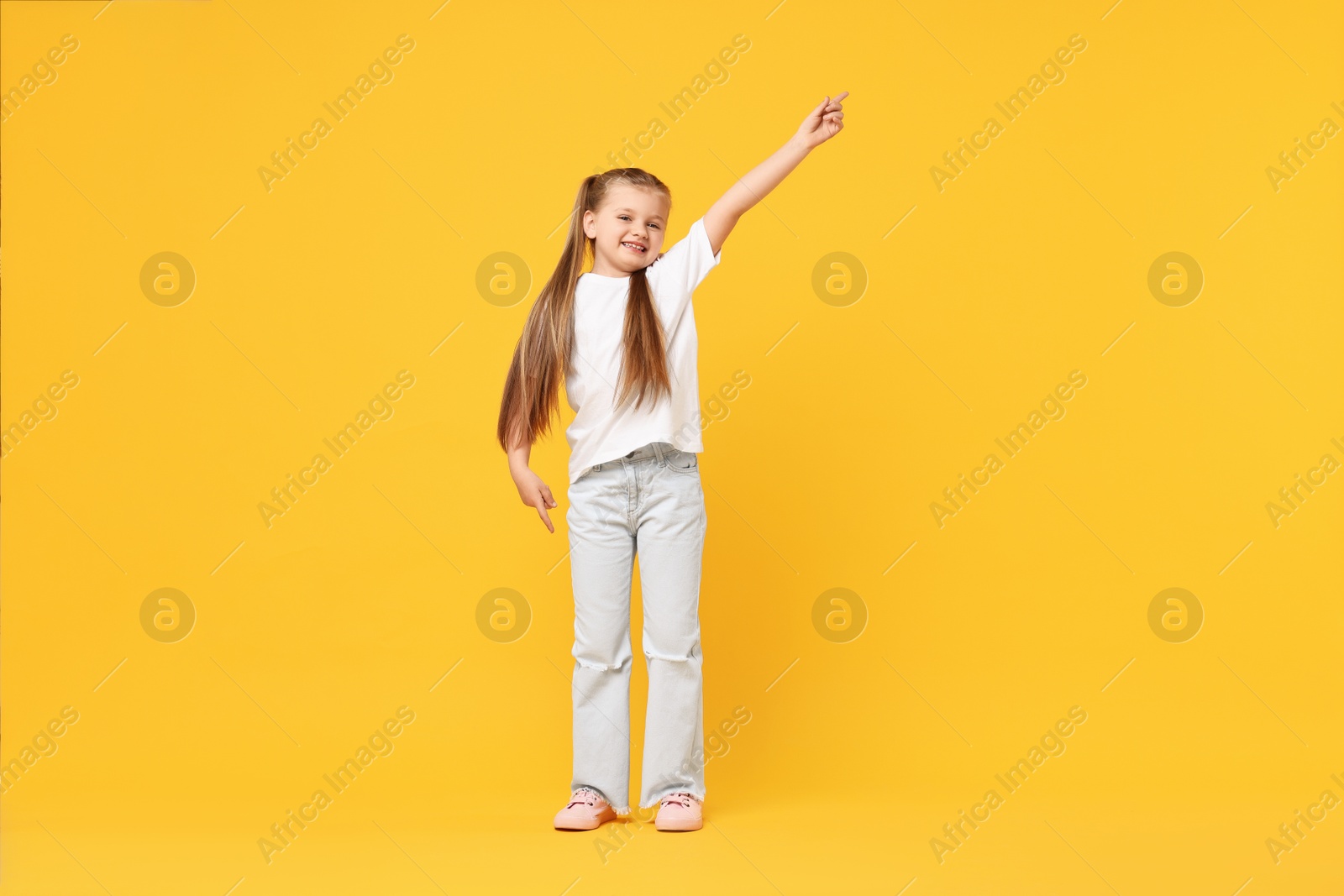 Photo of Cute little girl dancing on yellow background, space for text