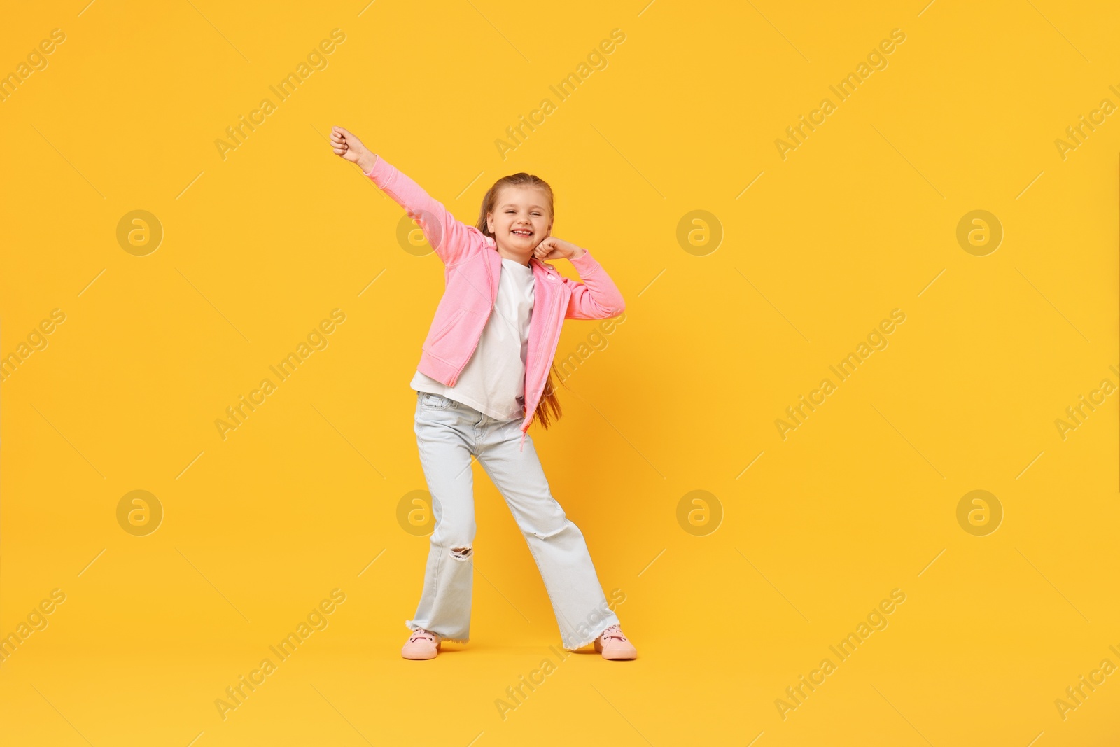Photo of Cute little girl dancing on yellow background, space for text