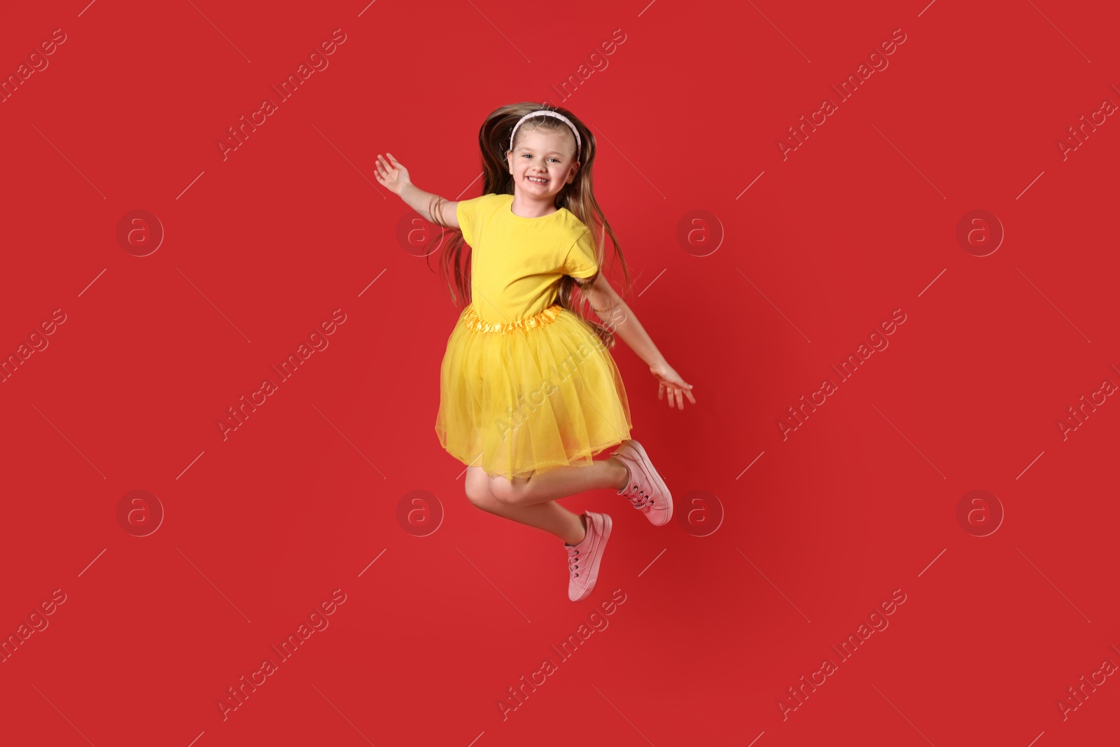 Photo of Cute little girl dancing on red background