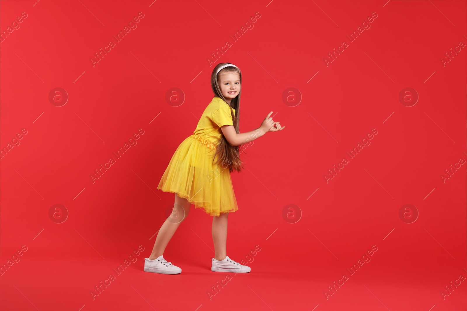 Photo of Cute little girl dancing on red background