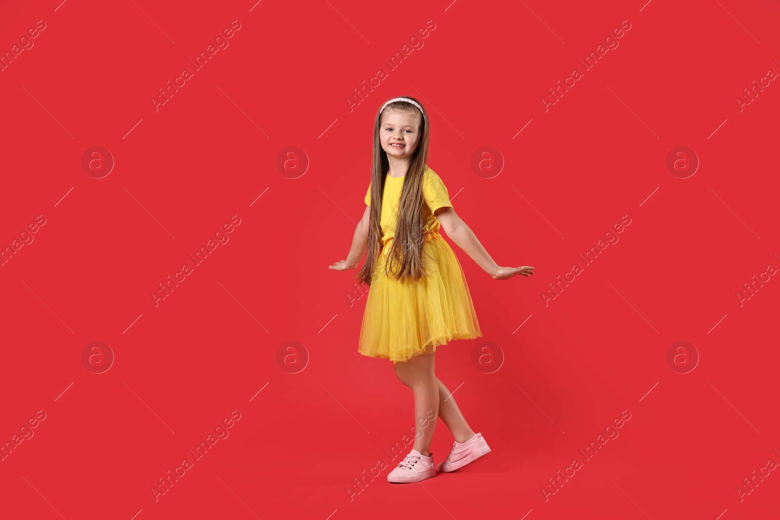 Photo of Cute little girl dancing on red background