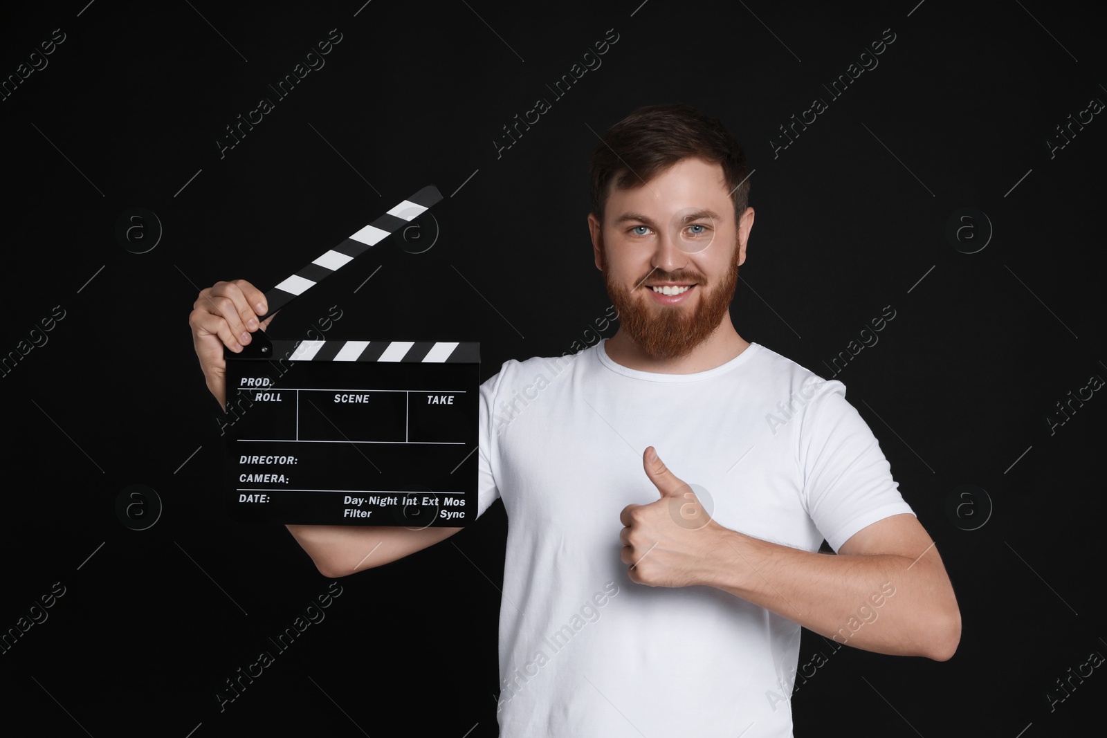 Photo of Making movie. Happy man with clapperboard showing thumb up on black background