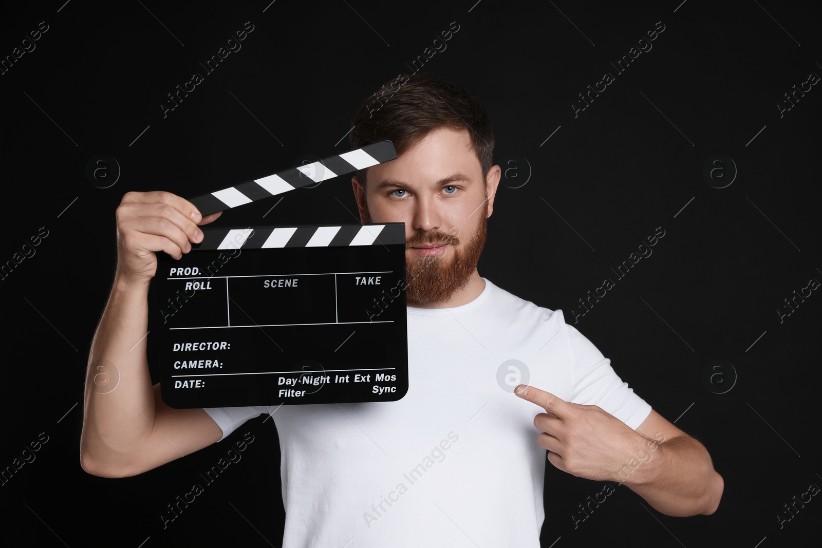 Photo of Making movie. Man pointing at clapperboard on black background