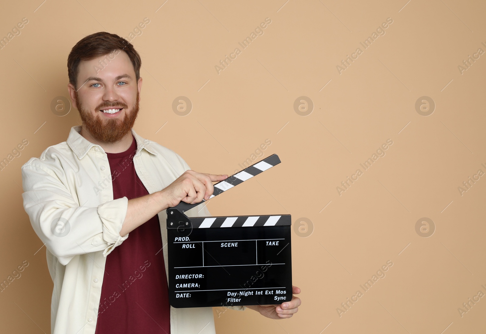 Photo of Making movie. Smiling man with clapperboard on beige background. Space for text