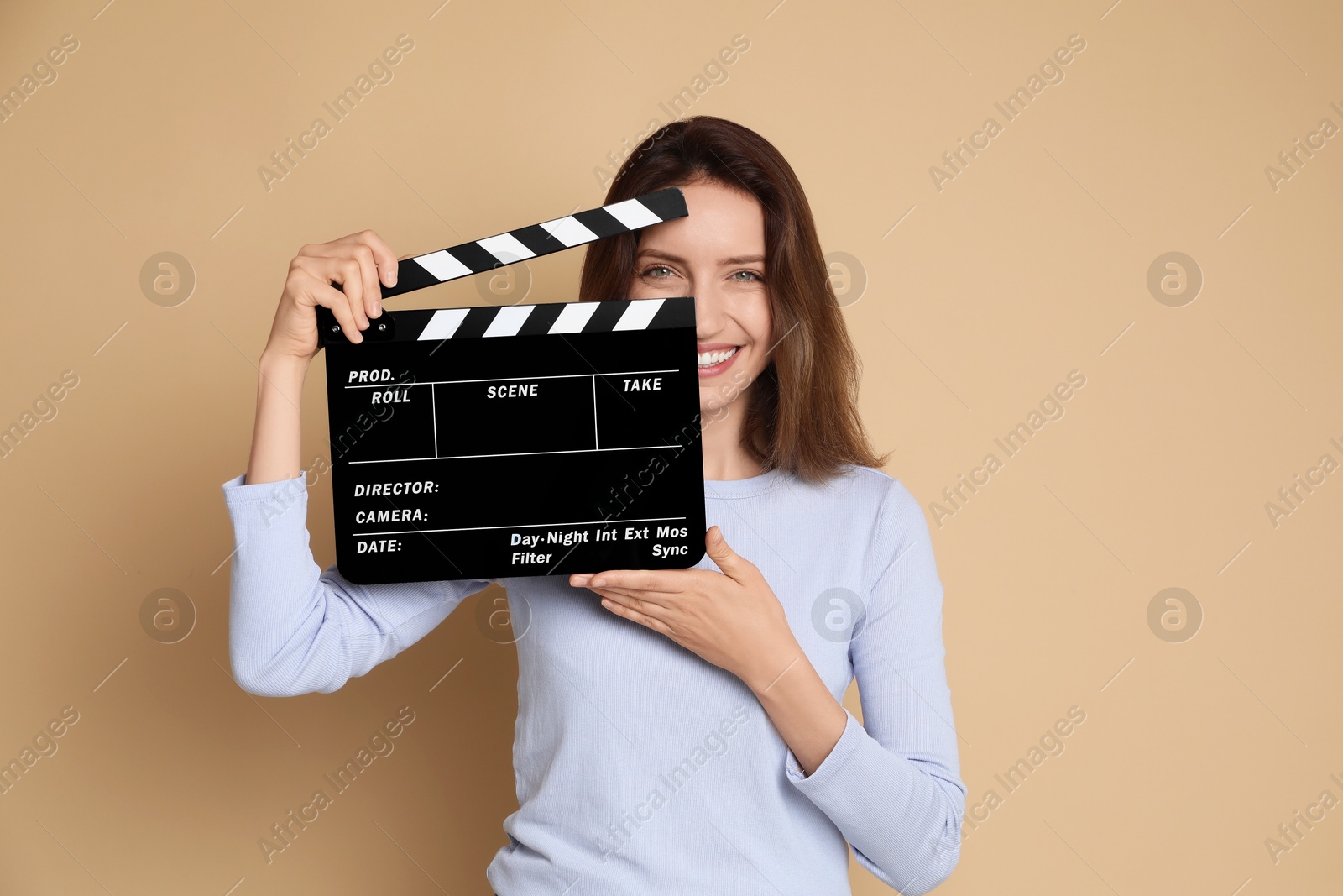 Photo of Making movie. Smiling woman with clapperboard on beige background