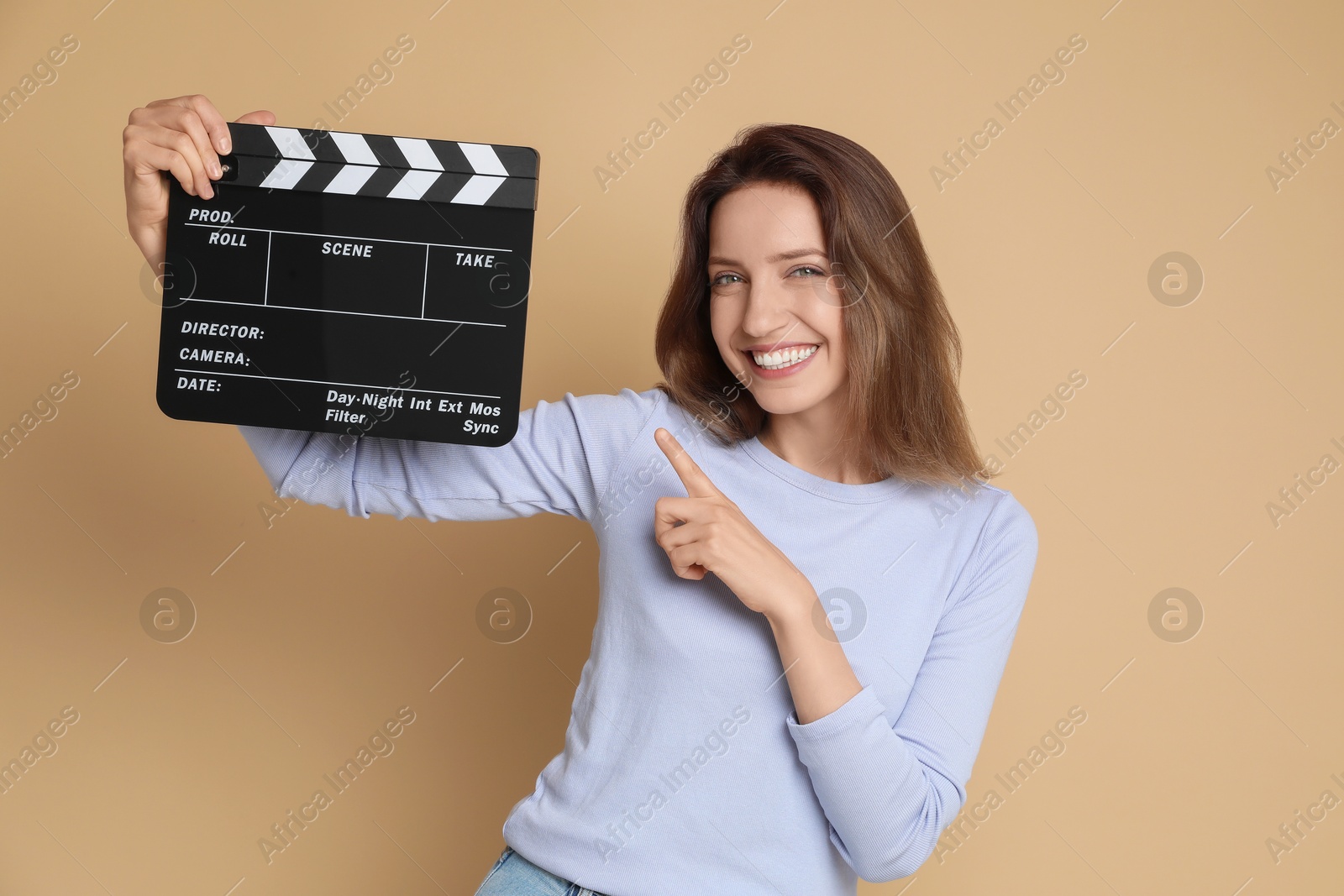 Photo of Making movie. Smiling woman pointing at clapperboard on beige background