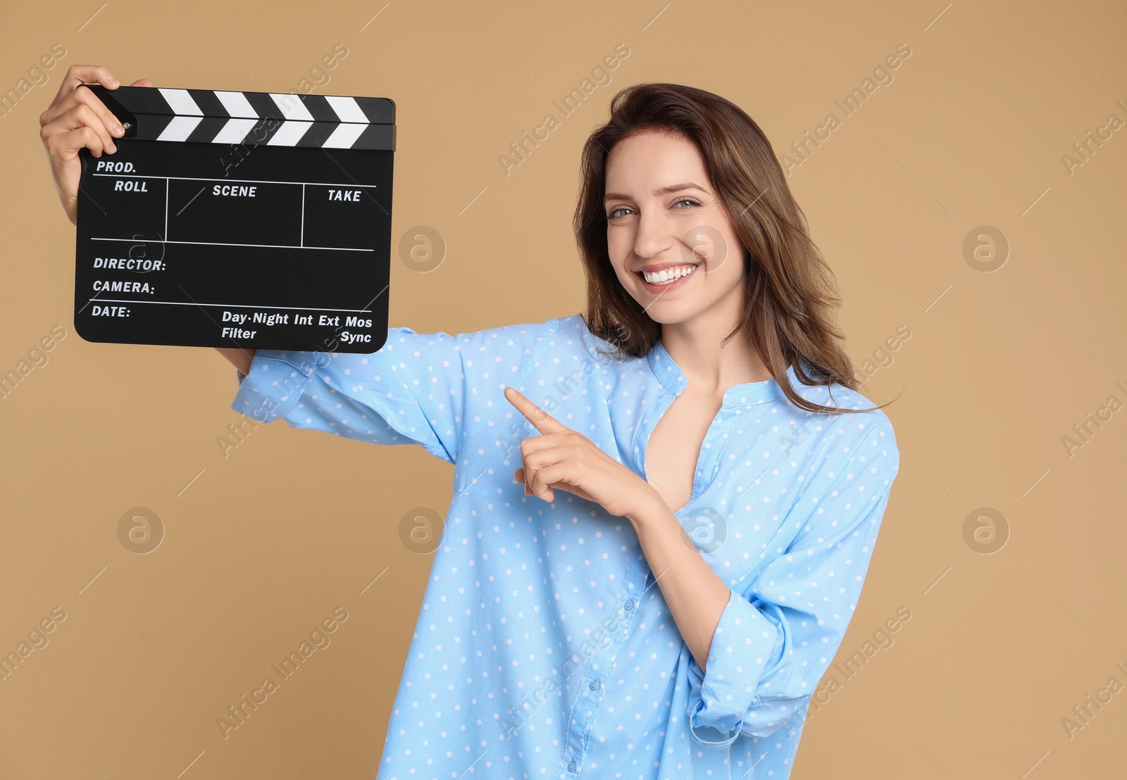 Photo of Making movie. Smiling woman pointing at clapperboard on beige background