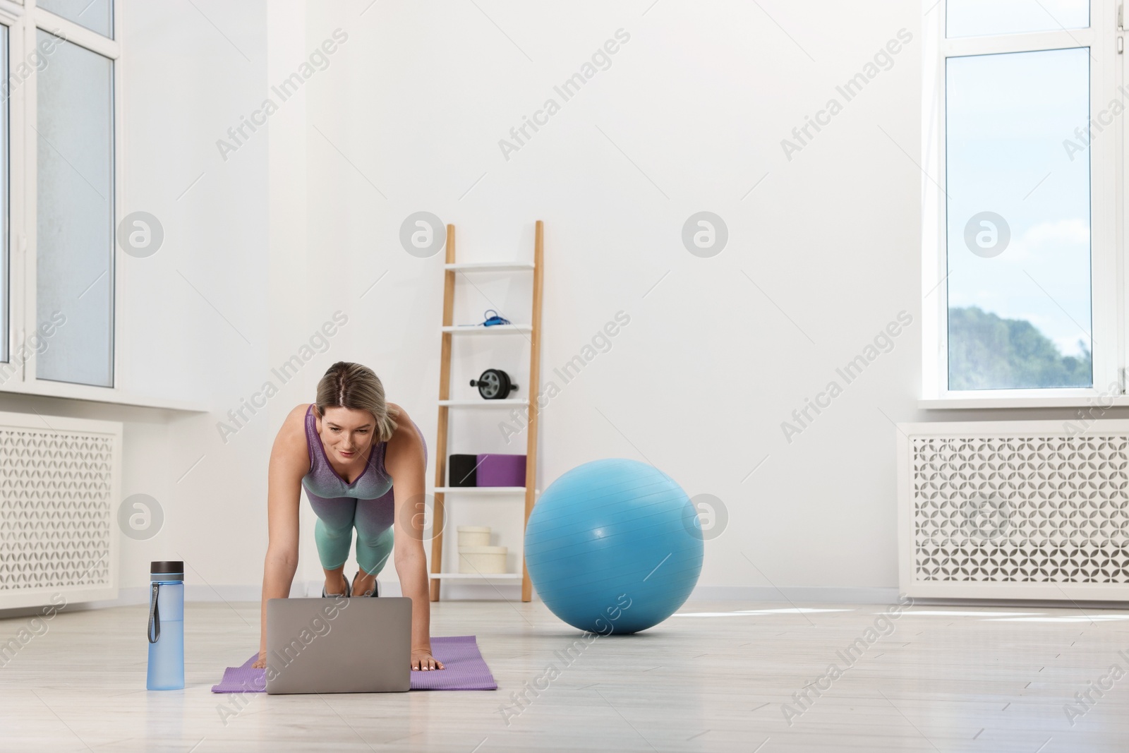 Photo of Online fitness trainer. Woman doing exercise near laptop at home