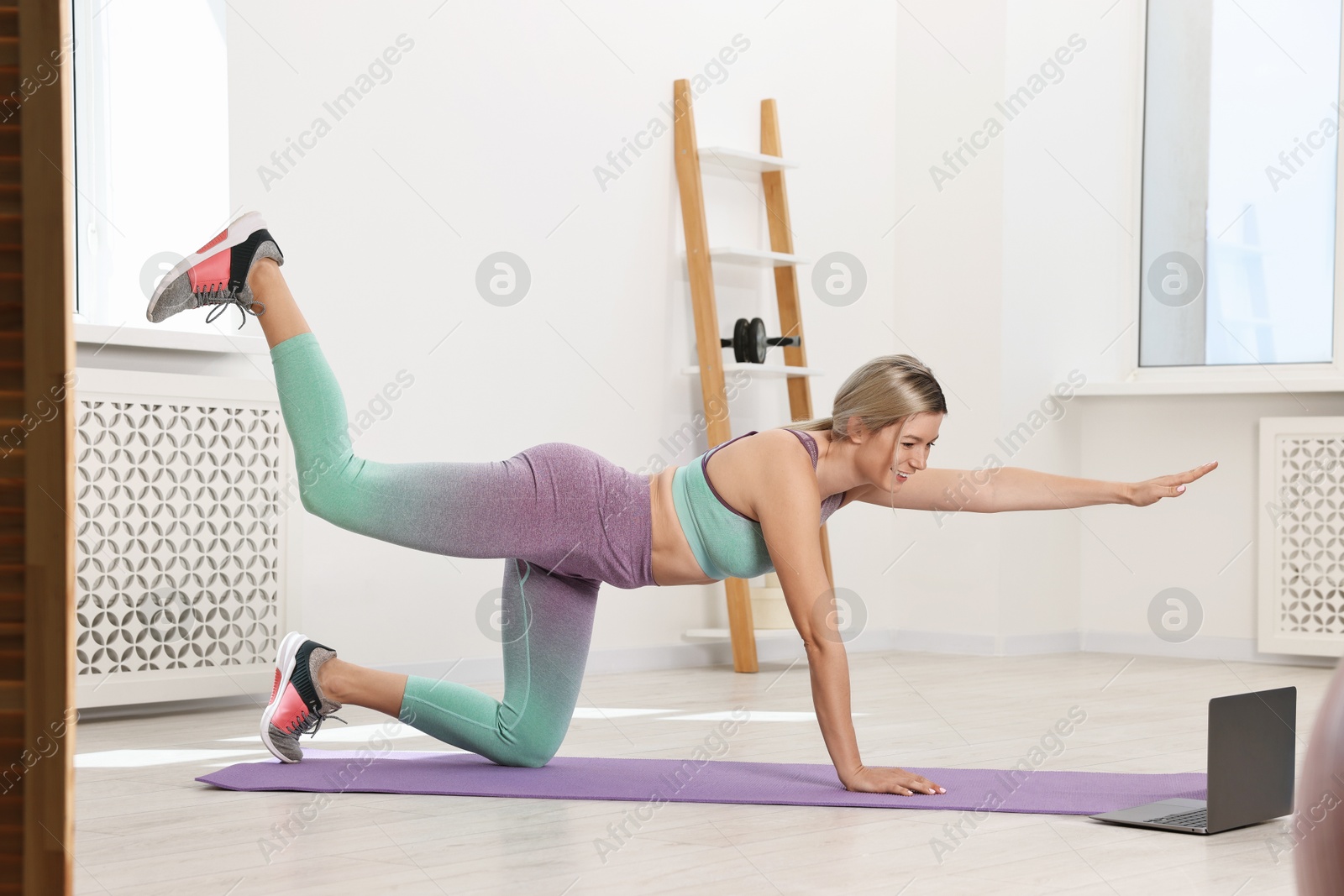 Photo of Online fitness trainer. Woman doing exercise near laptop at home