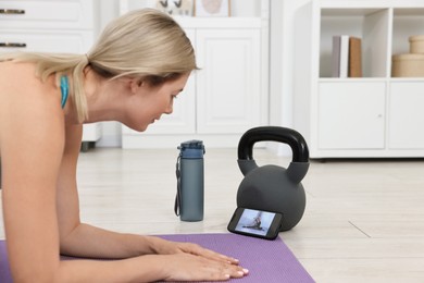 Photo of Online fitness trainer. Woman doing exercise near smartphone at home