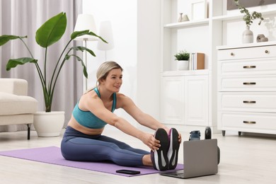 Photo of Online fitness trainer. Woman doing exercise near laptop at home