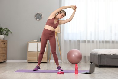 Online fitness trainer. Woman stretching near laptop at home