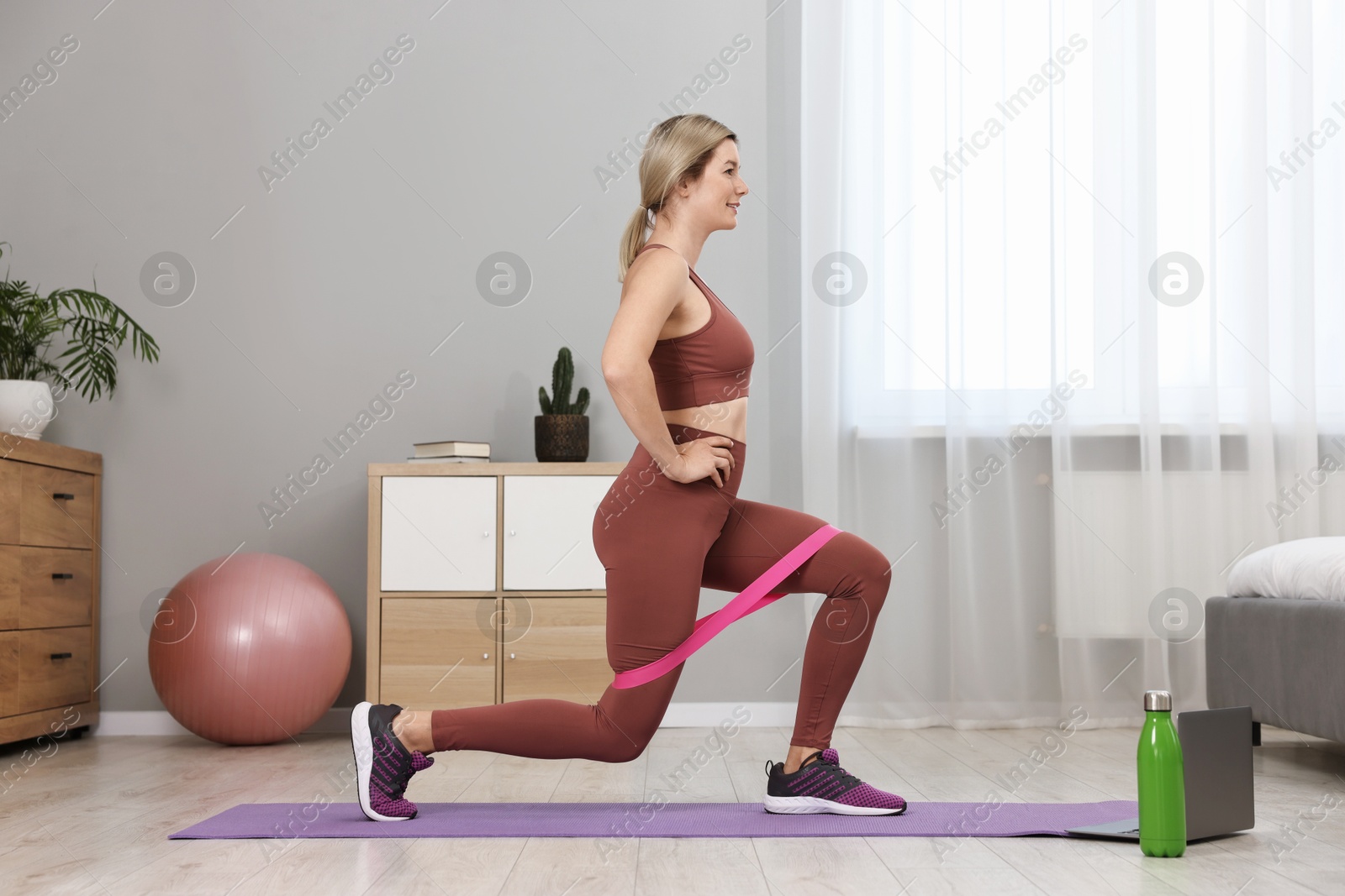 Photo of Online fitness trainer. Woman doing exercise with elastic band near laptop at home