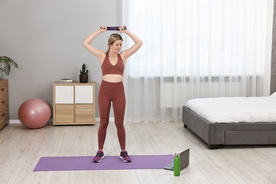 Online fitness trainer. Woman doing exercise with elastic band near laptop at home