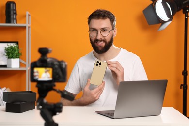 Photo of Smiling technology blogger with camera recording video review about smartphone at home