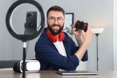 Photo of Smiling technology blogger with game controller recording video review at home