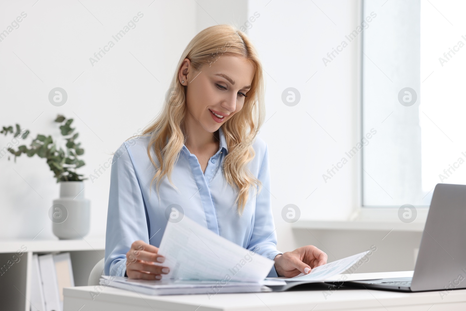 Photo of Happy secretary working with documents at table in office