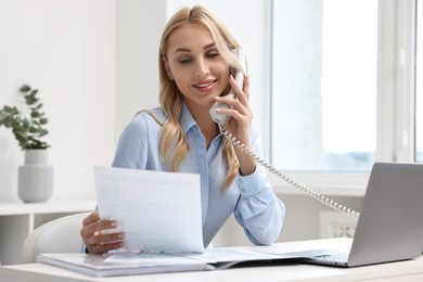 Happy secretary with document talking on phone in office